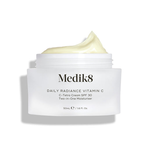Na zdjęciu widać otwarty szklany słoiczek z kremem Medik8 Daily Radiance Vitamin C, na którego powierzchni widoczna jest spora warstwa jasnożółtego kremu. Napis informuje, że jest to krem nawilżający 2 w 1 C-Tetra Cream SPF 30 o pojemności 50 ml.