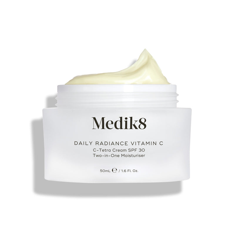 Na zdjęciu widać otwarty szklany słoiczek z kremem Medik8 Daily Radiance Vitamin C, na którego powierzchni widoczna jest spora warstwa jasnożółtego kremu. Napis informuje, że jest to krem nawilżający 2 w 1 C-Tetra Cream SPF 30 o pojemności 50 ml.