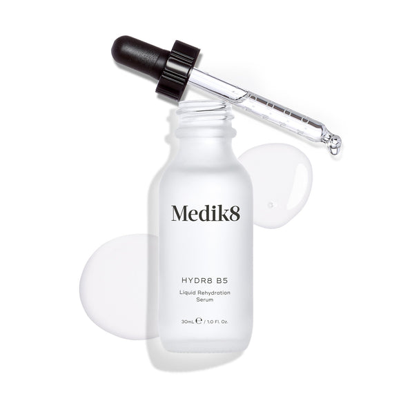 Butelka serum Medik8 Hydr8 B5 stoi na czystym białym tle, na którym widoczna jest kałuża przezroczystego płynu oraz krople, a na górze spoczywa zakraplacz. Napis informuje, że jest to płynne serum nawilżające o pojemności 30 ml.-27