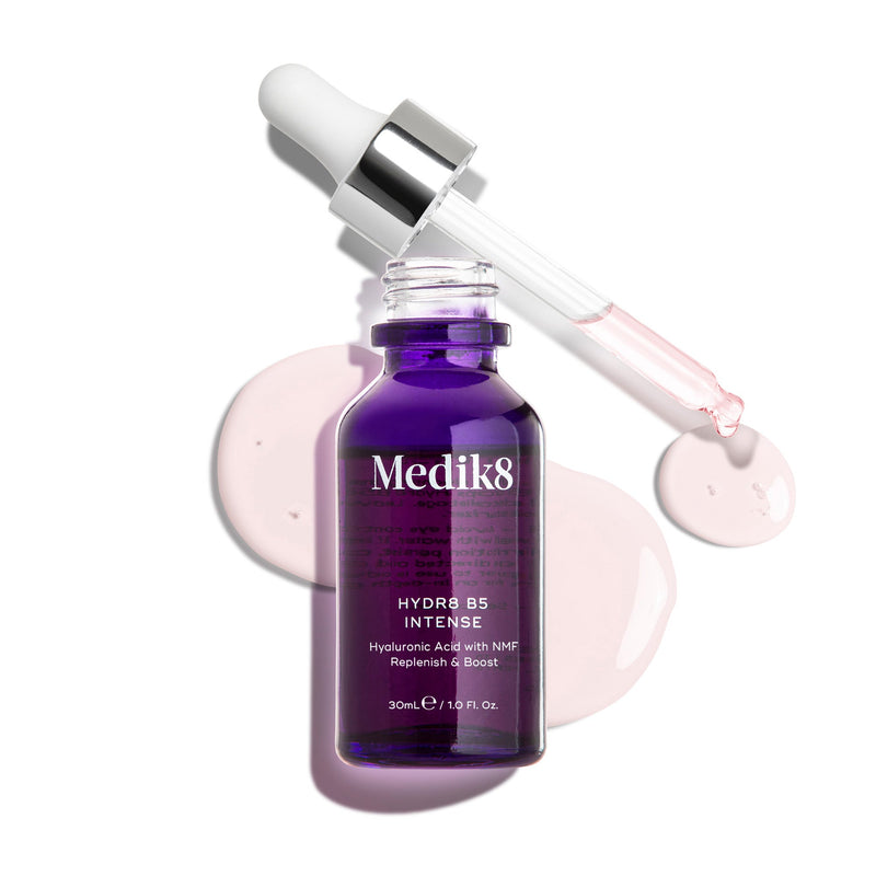 Fioletowa szklana butelka z pipetą Medik8 Hydr8 B5 Intense przedstawiona na czystym białym tle, z otwartą pipetą umieszczoną nad jasnoróżowymi kroplami serum. Tekst podkreśla, że formuła zawiera kwas hialuronowy oraz NMF (Natural Moisturising Factors), które pomagają nawilżać i wzmacniać skórę, w rozmiarze 30 ml.
