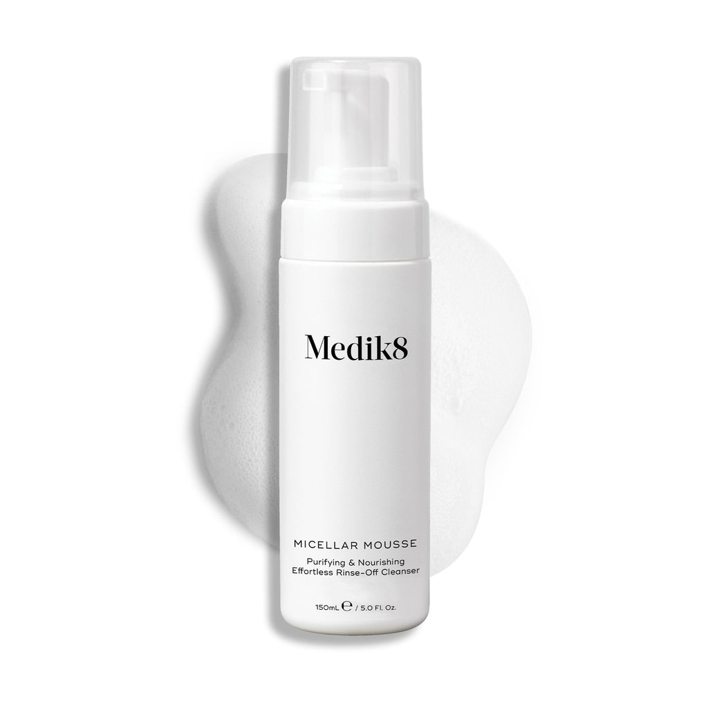Butelka z pompką Medik8 Micellar Mousse na białym tle z widoczną smugą białej pianki za produktem, podkreślającą jego konsystencję.
