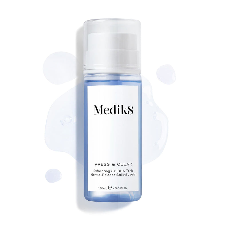 Butelka Medik8 Press & Clear (150 ml) na białym tle z rozbryzgami niebieskiego toniku wokół produktu. Grafika podkreśla formułę złuszczającego toniku z 2% BHA.
