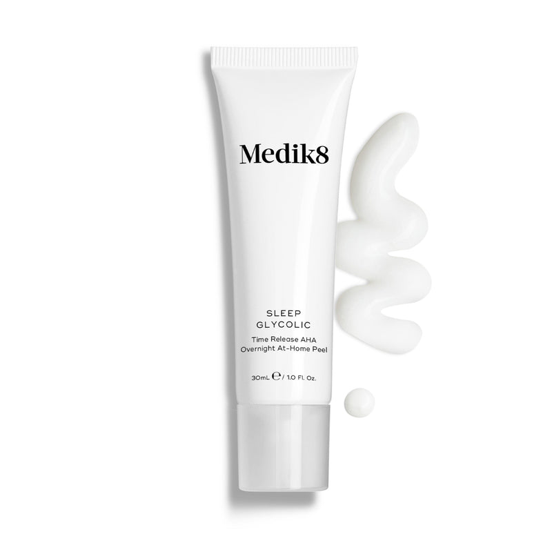 Butelka Medik8 Sleep Glycolic stoi na czystym białym tle z falistą smugą oraz małą kroplą białej konsystencji kremu. Tekst identyfikuje produkt jako 30 ml nocny peeling AHA o przedłużonym uwalnianiu do stosowania w domu.
