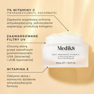 Szklany słoiczek z produktem Medik8 Daily Radiance Vitamin C na tle w ciepłym złotym odcieniu, z opisem składników. Tekst podkreśla zawartość 7% witaminy C (askorbinianu tetraheksylodecylowego), zapewniającej ochronę antyoksydacyjną i wspomagającą produkcję kolagenu, wysokiej jakości filtrów UV chroniących przed promieniowaniem UVA i UVB oraz witaminy E, która odżywia skórę i wzmacnia działanie przeciwutleniające.