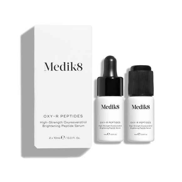 Dwie małe białe butelki serum Oxy-R Peptides są zaprezentowane na białym tle. Obok leży czarna pipeta, a na powierzchni widoczne są dwie krople żółtego serum.
-36
