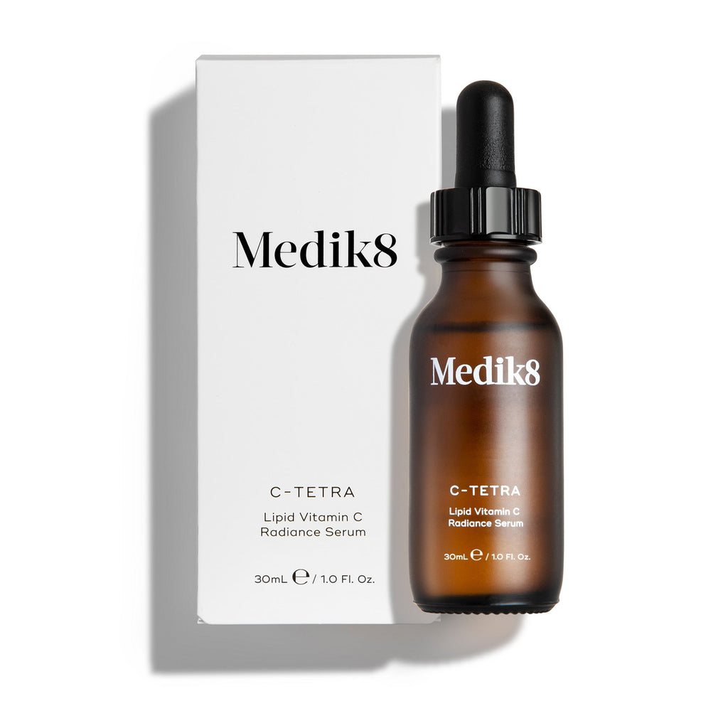 Bursztynowa szklana butelka serum Medik8 C-Tetra lipid vitamin C radiance serum przedstawiona obok białego kartonowego opakowania. Oba elementy umieszczone są na czystym białym tle z delikatnym cieniem.
