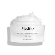Słoiczek z kremem Medik8 Advanced Night Restore przedstawiony w pozycji otwartej, z obfitą porcją białego kremu uformowaną w kopczyk na wierzchu, na tle czystej bieli, co podkreśla jego gładką, regenerującą konsystencję. Na słoiczku widnieje czarny napis: „Rejuvenating Multi-Ceramide Night Cream”.