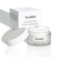 Otwarty matowy szklany słoiczek Medik8 Total Moisture Daily Facial Cream z białą zakrętką umieszczoną obok, prezentujący bogaty biały krem. Słoiczek stoi przed białym kartonowym opakowaniem na jasnym tle. Tekst na obu opakowaniach brzmi: „AM/PM wielowarstwowe nawilżenie z H.E.O.® i prebiotycznymi peptydami”.
