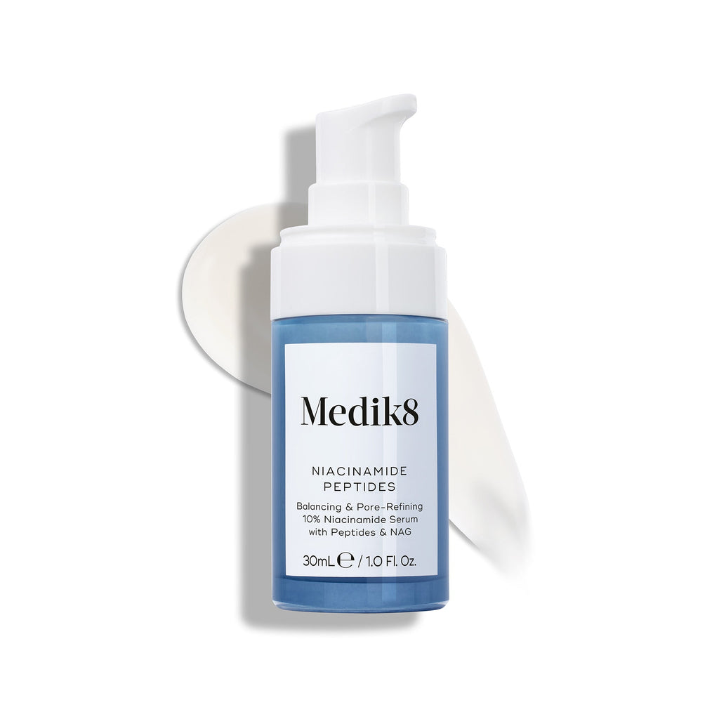 Butelka serum Medik8 Niacinamide Peptides z białą pompką, stojąca na białej powierzchni, za którą widoczna jest smuga białego serum.