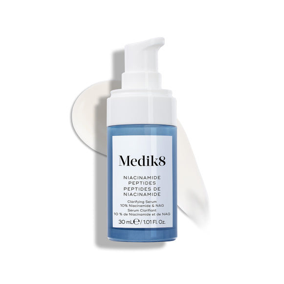 Butelka serum Medik8 Niacinamide Peptides z białą pompką, stojąca na białej powierzchni, za którą widoczna jest smuga białego serum.-24